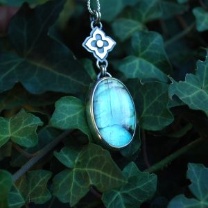 Pendentif en argent 925 avec cabochon de labradorite aux reflets bleus et motif floral en argent au-dessus de la pierre.